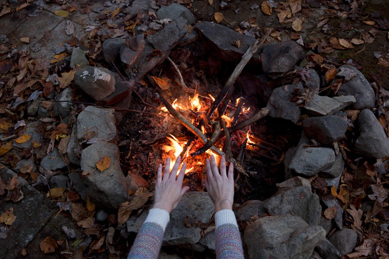 Woman warming her hands by a campside fire she has made herself