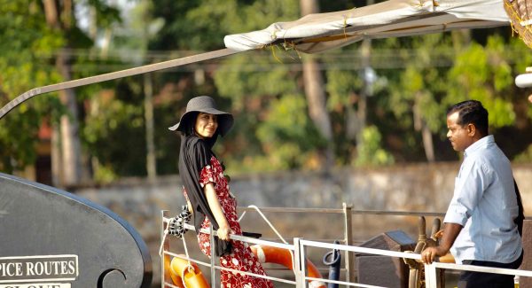Woman looks at camera while on houseboat. Man opposite woman looks at river.