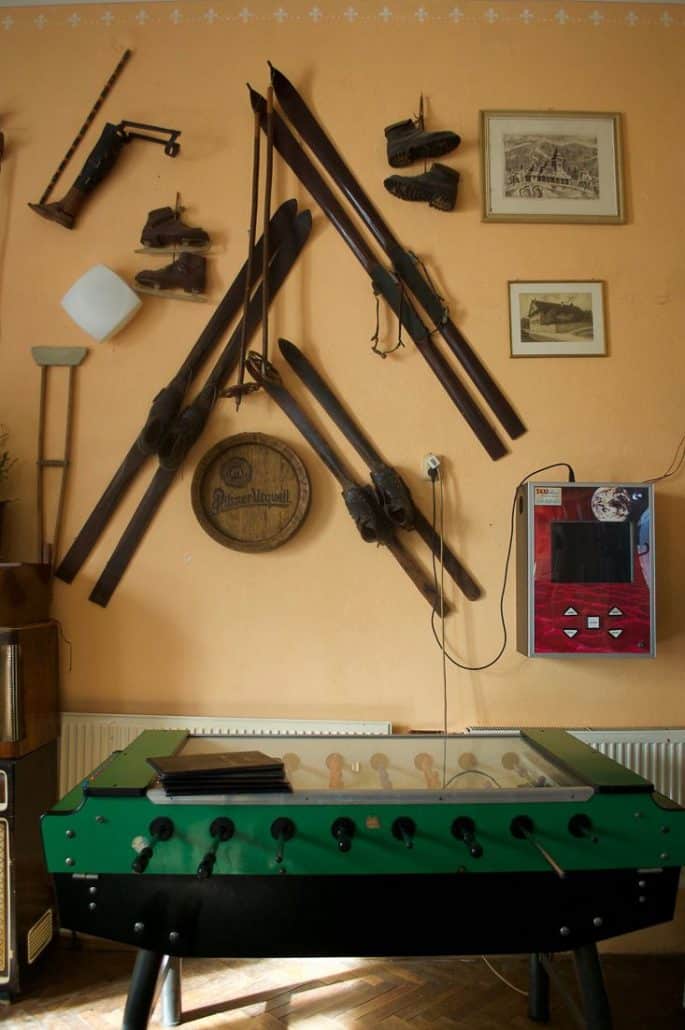 Photo inside a chalet showing some vintage ski equipment that is hung on the wall as well as an old foosball table in front.