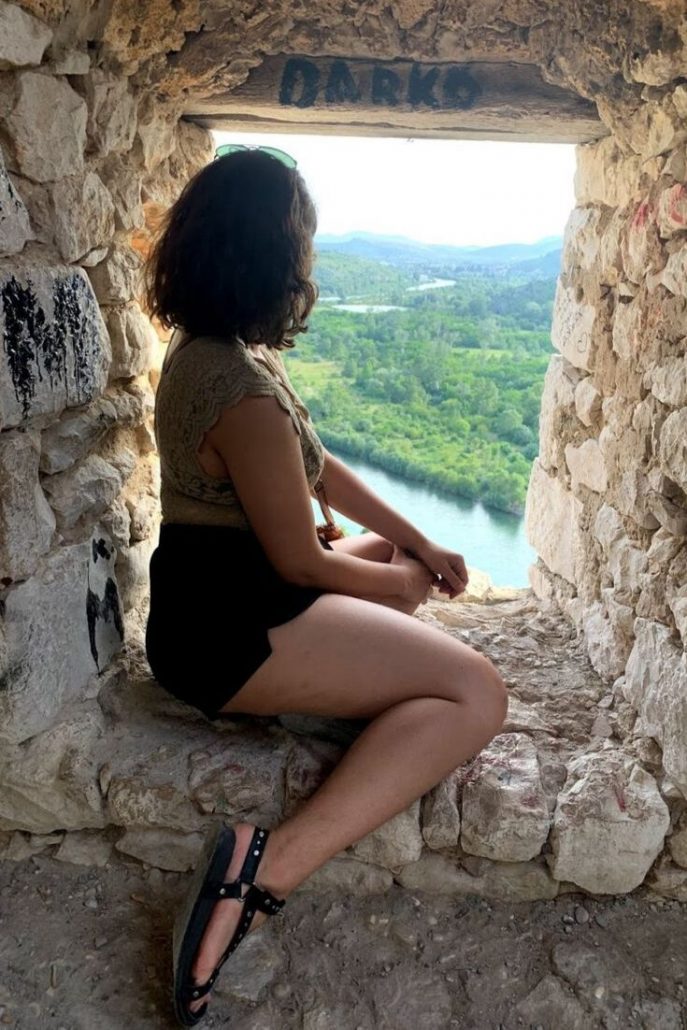 Gigi sitting in a window looking out to the Mostar, which is filled with lush forests.