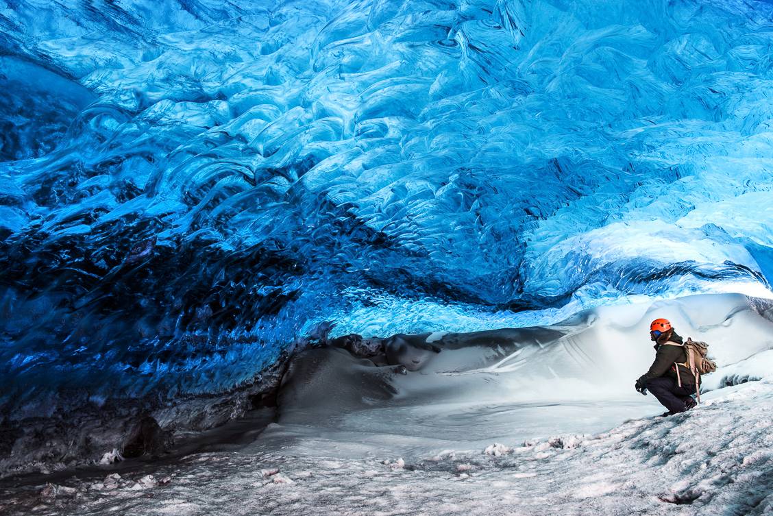 Photos of a person crouching down beneath a wall of ice in Iceland