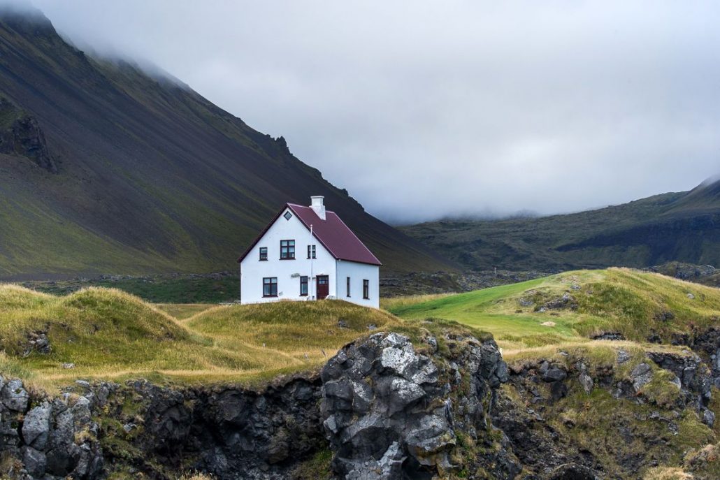 Photo of a lone white house surrounded by rolling hills in Iceland