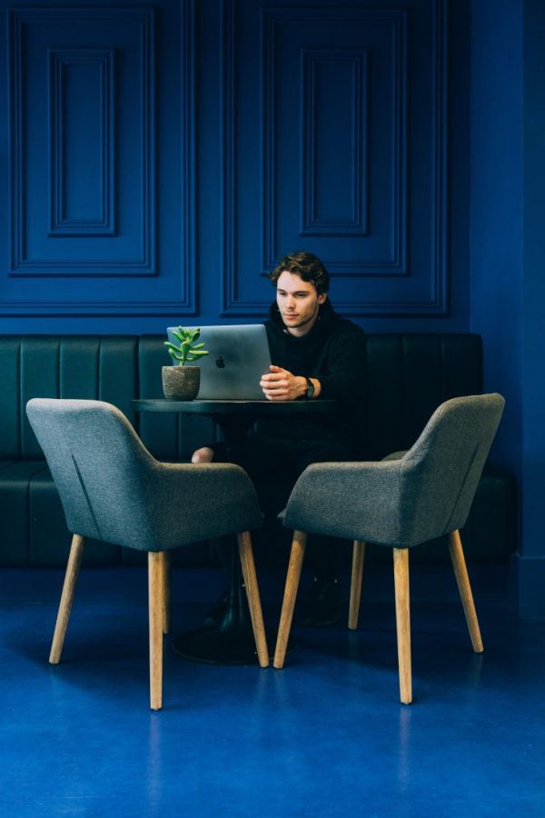 Photo of a man working on his laptop in a blue cafe that features a blue wall, blue floor, and blue chairs.