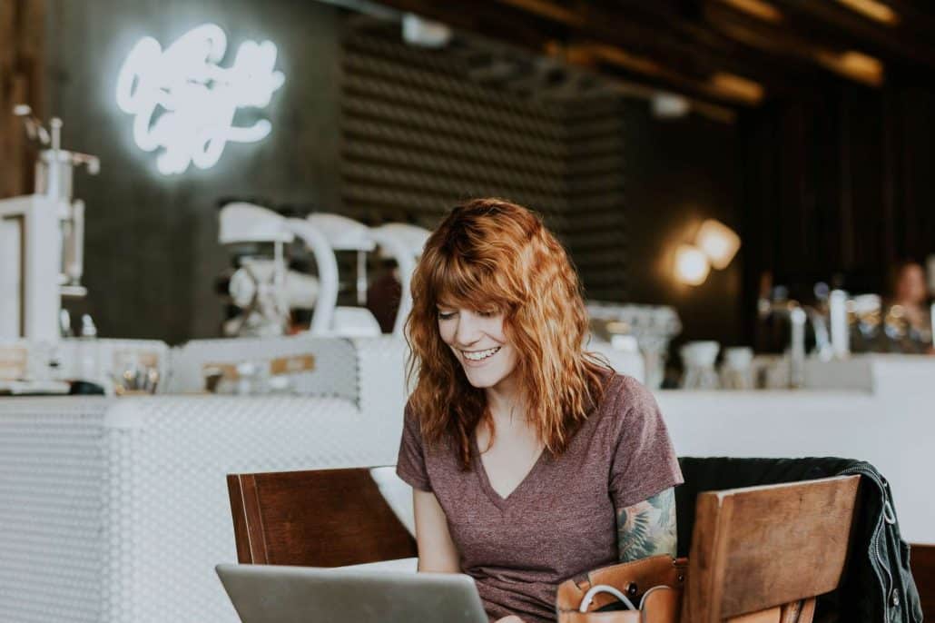 A tattooed woman sitting in a cafe and looking at laptop