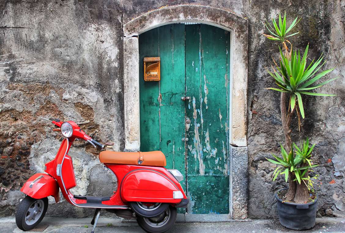 Photo of a read vespa parked in front of an old green door in Italy