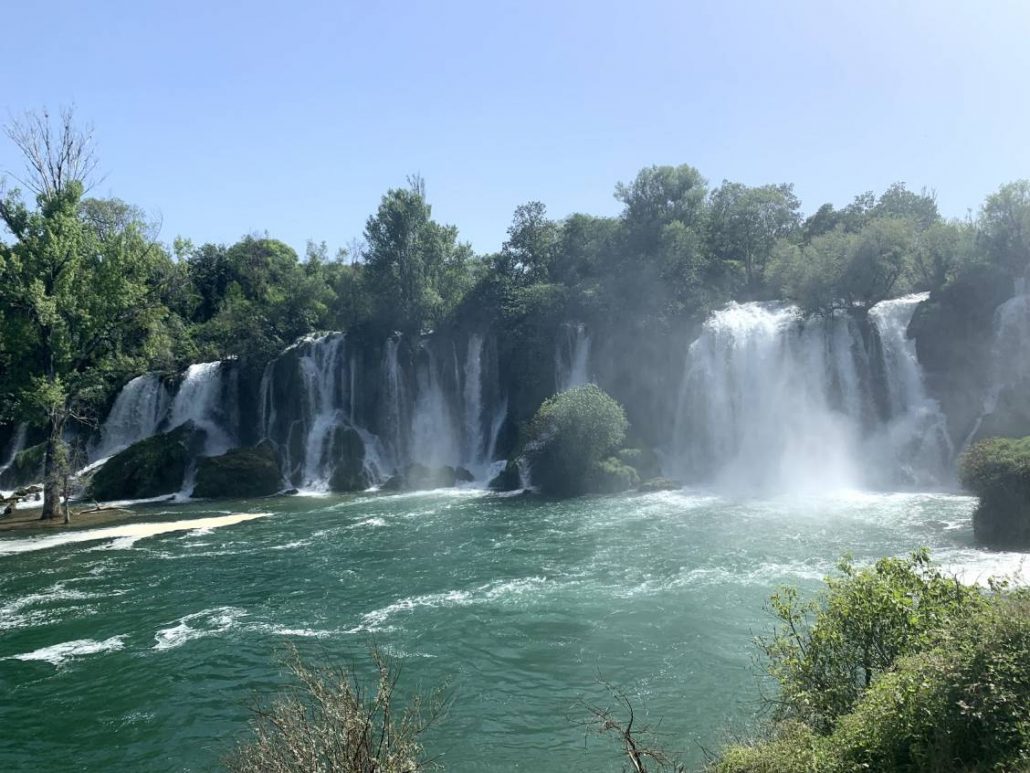 A view of Kravice Falls where you can see about 15 cascades lined up next to each other all emptying into one pool.
