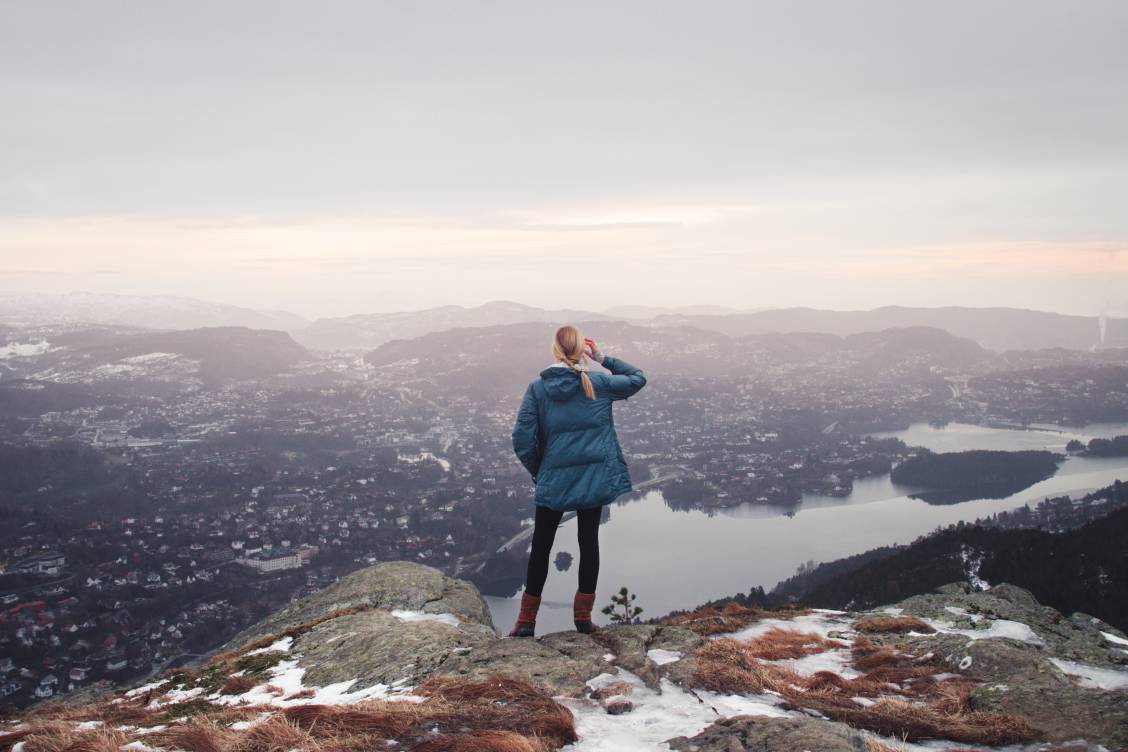 Photo of a blonde woman in a blue jacket looking out at a viewpoint atop Løvstakken in Bergen, Norway