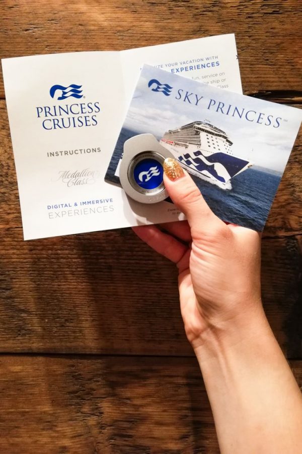 Princess Cruises Ocean Medallion being held in the hand along with the Medallion Class instruction manual