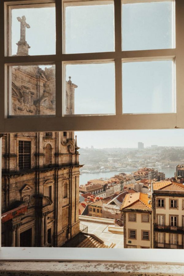 Photo taken from a window looking out the city of Portugal with an old cathedral in the foreground.