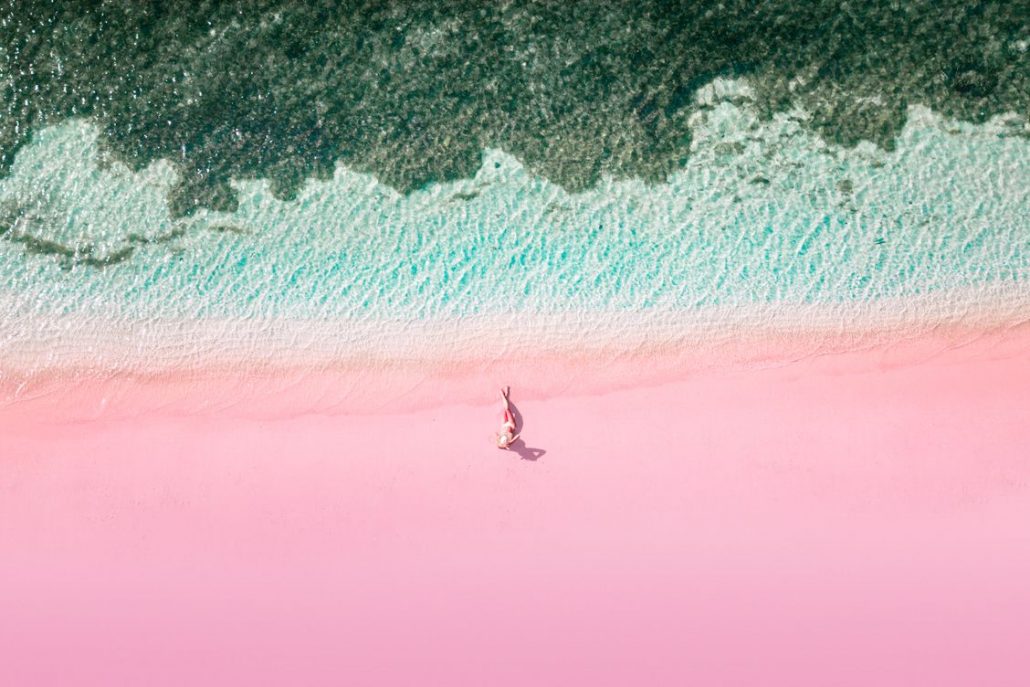 Aerial view of a solo female traveller lying down on the pink beach in Indonesia