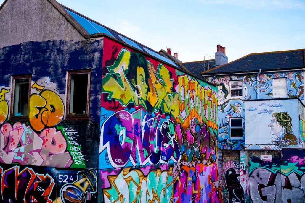 Graffiti and street art mix in vibrant colours on the back of houses in the backstreets of Brighton