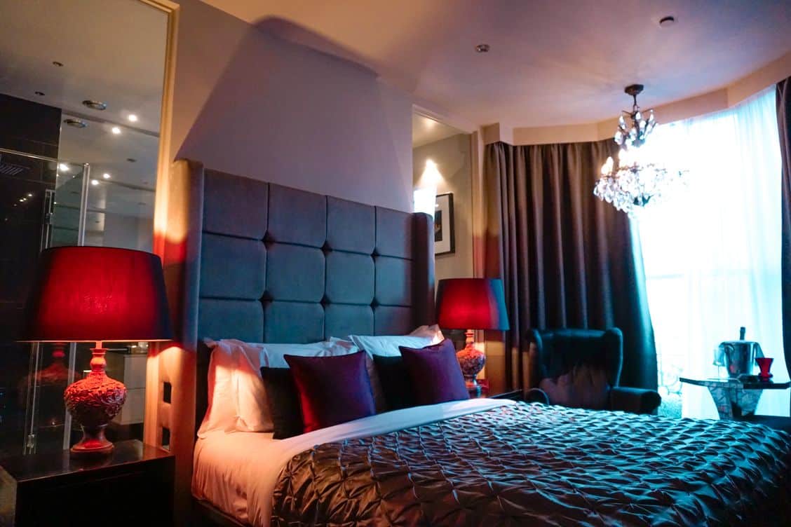 Deep red plush king-sized bed with deep red lampshades and a chandelier at The Square Hotel Brighton