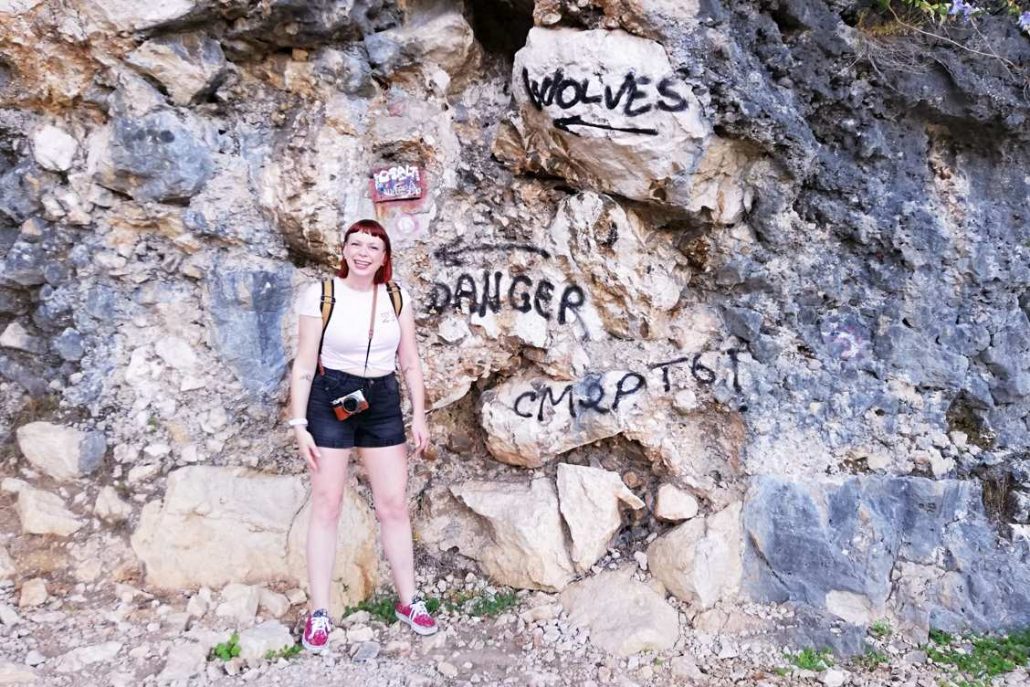 Photo of Alice in front of a rock face with graffiti warning about wolves in the area