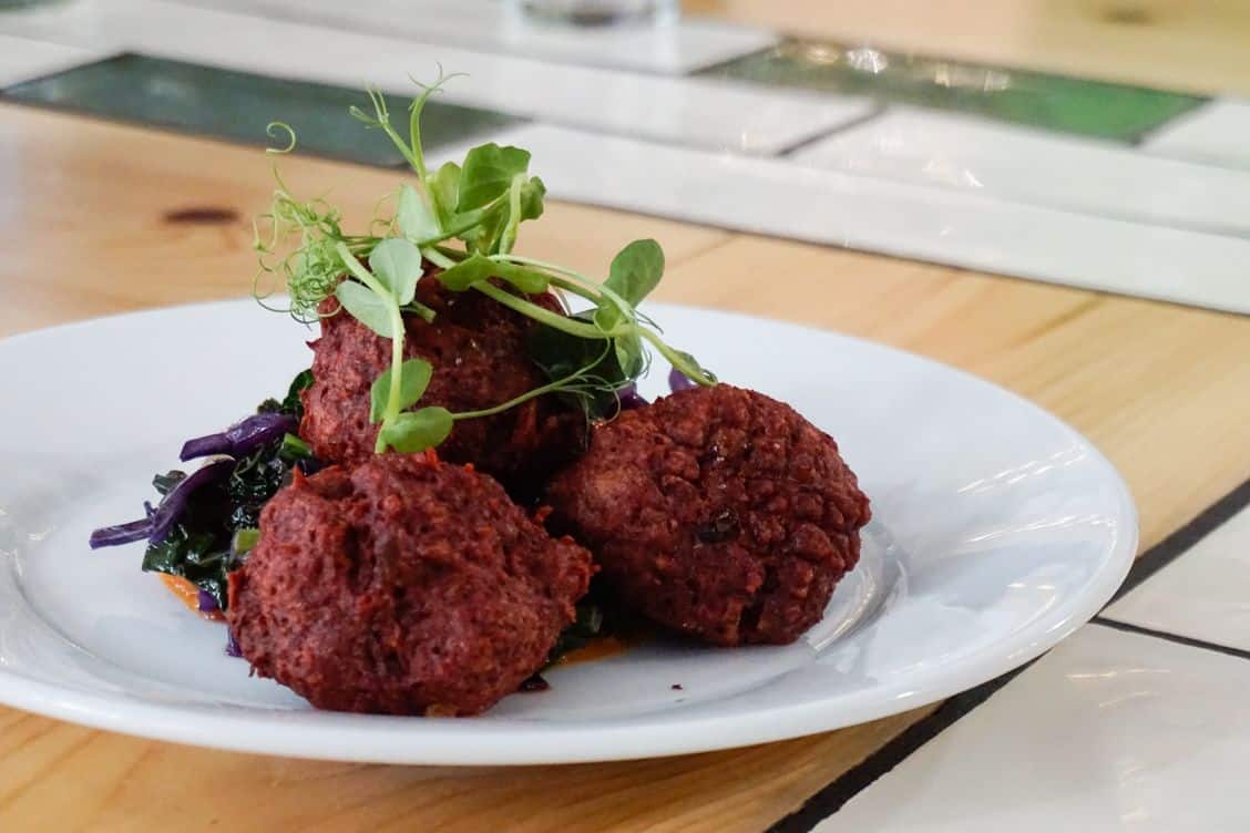 Beetroot falafel topped with green herbs on a white plate at Eat Your Greens Leeds
