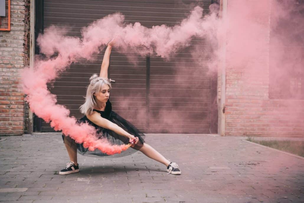 Woman in black dress and sneakers dancing on the street with pink smoke