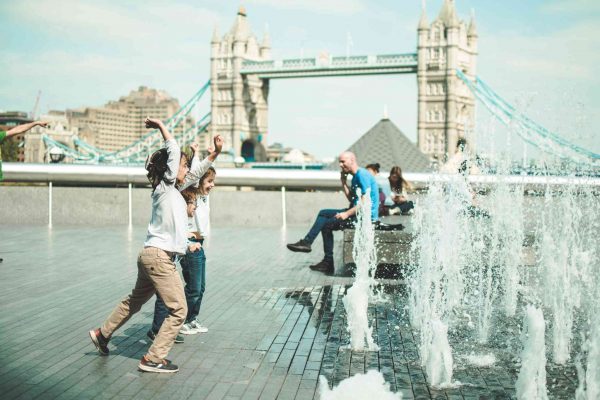Kids playing in London with water fountains in front of Tower Bridge during a London visit with kids