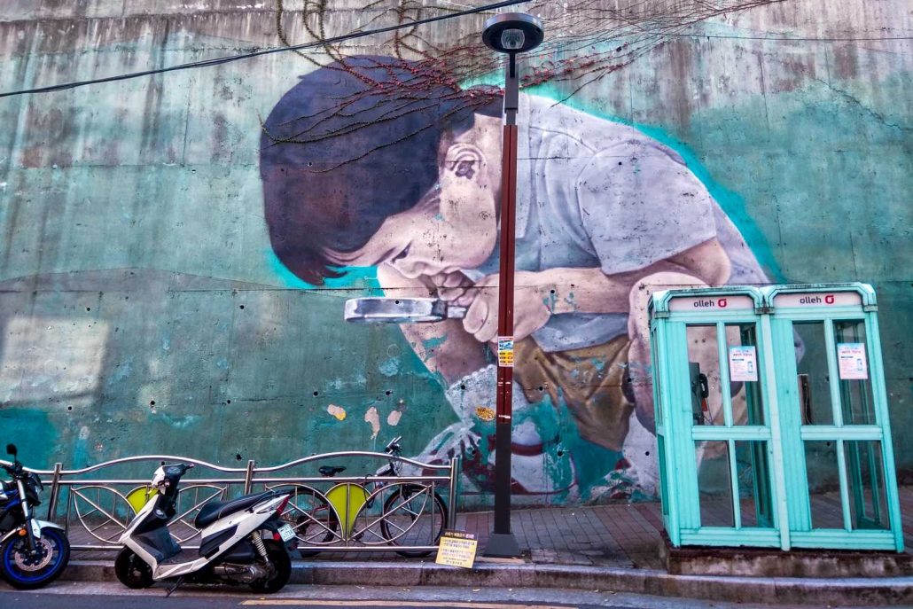 Street art in Busan of a young Korean child using a looking glass to inspect what is on the street
