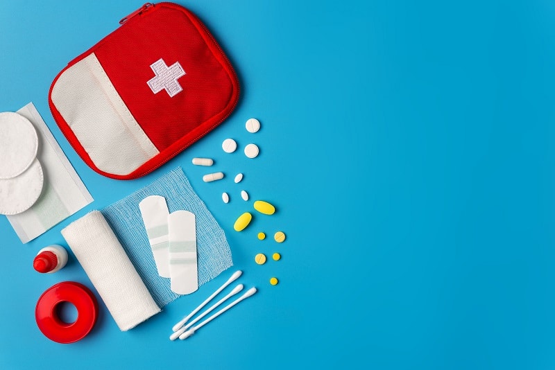 A red first aid kit for travel containing medicine, band aids, bandages and swabs