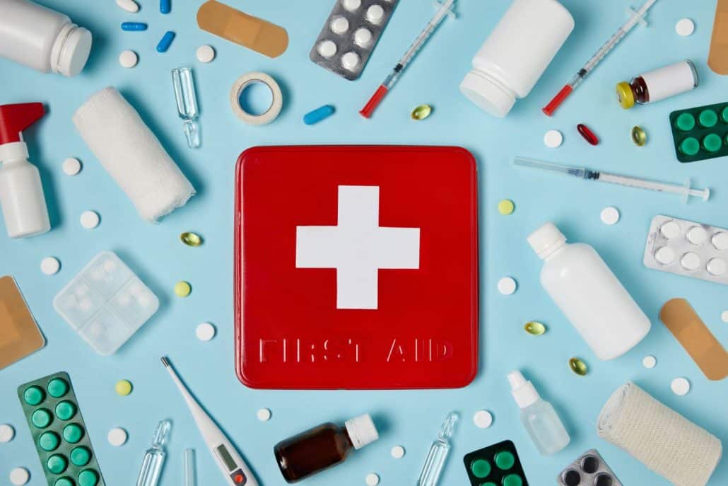 A red travel medicine kit surrounded by first aid supplied and travel medicine on a blue background