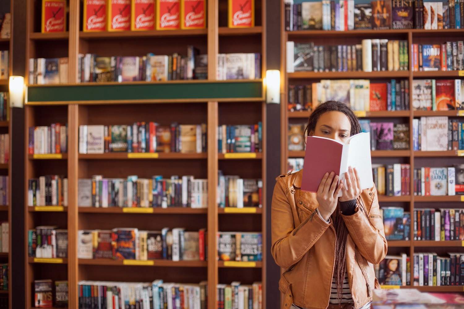 10 Best Travel Books of All Time with a lady peeking into a book in a colourful bookshop with lots of books behind her