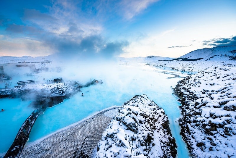 A dramatic view of the Blue Lagoon in Iceland with clouds and snow around the spa.