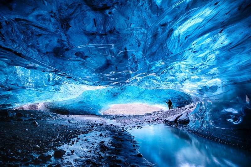 A man is taking a photo demonstrating the scale of the Breioarmerkurjokull ice cave in Iceland