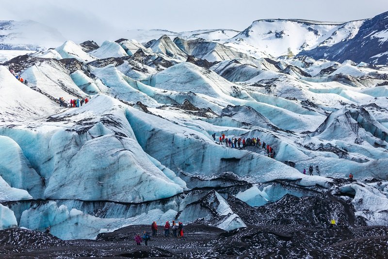 The thrilling Glacier of Solheimajokull in Iceland with beautiful tones of blue throughout it and a group hiking on its surface